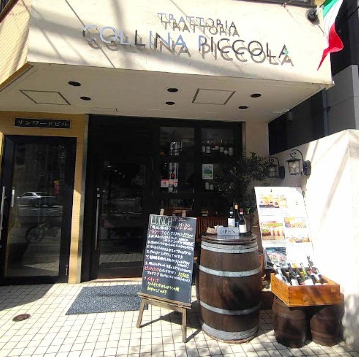 イタリア国旗がはためきく店舗前。ワイン樽とメニューの看板が目を引きます。