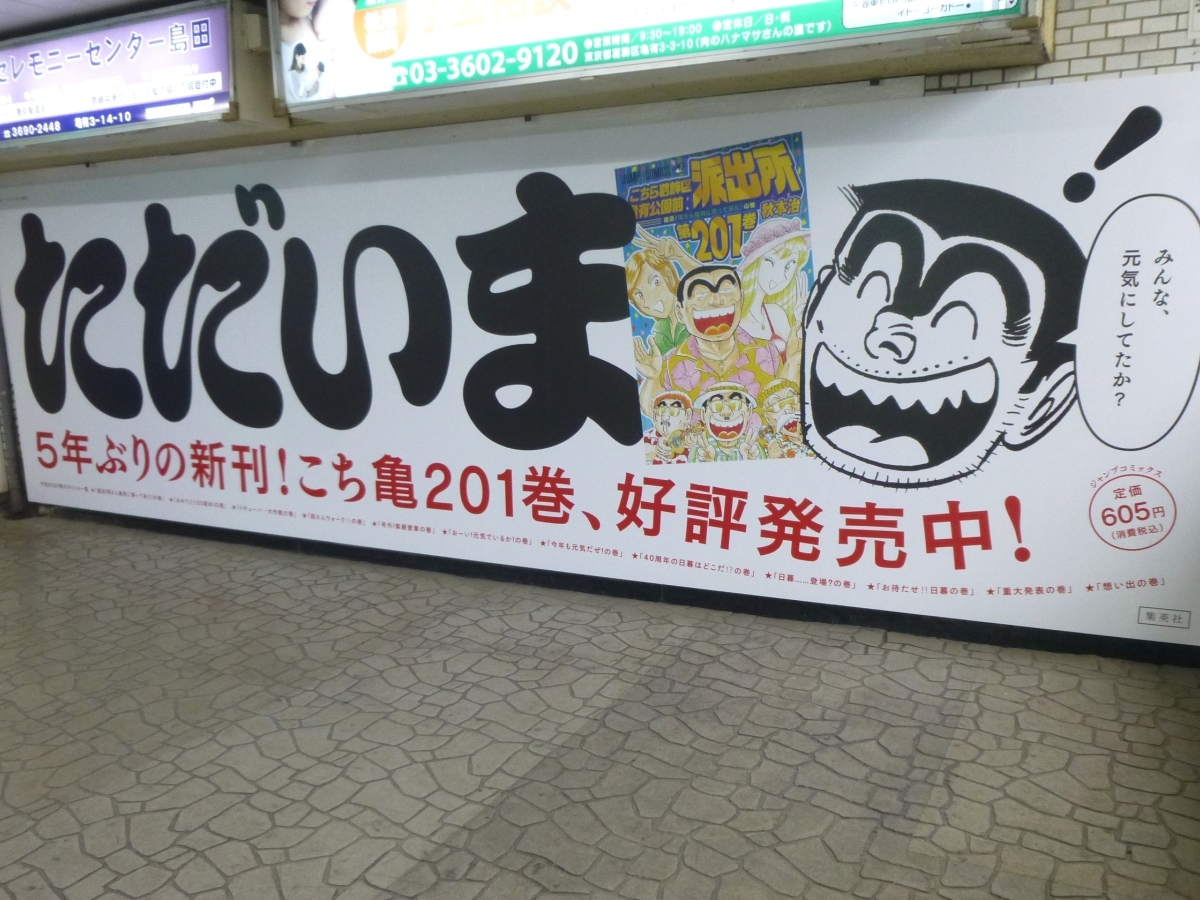 亀有駅の中二階連絡通路に現れた『こち亀』201巻の壁面広告。大きい！