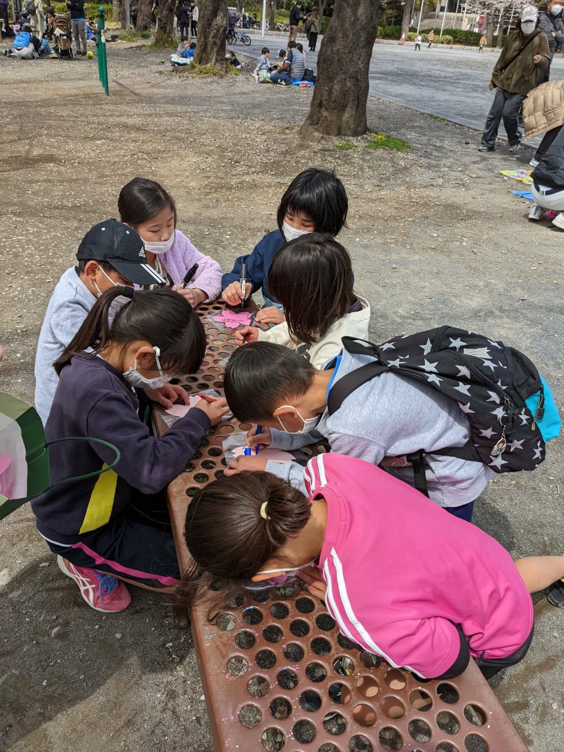 集まって桜の花びらに言葉を書く子どもたち