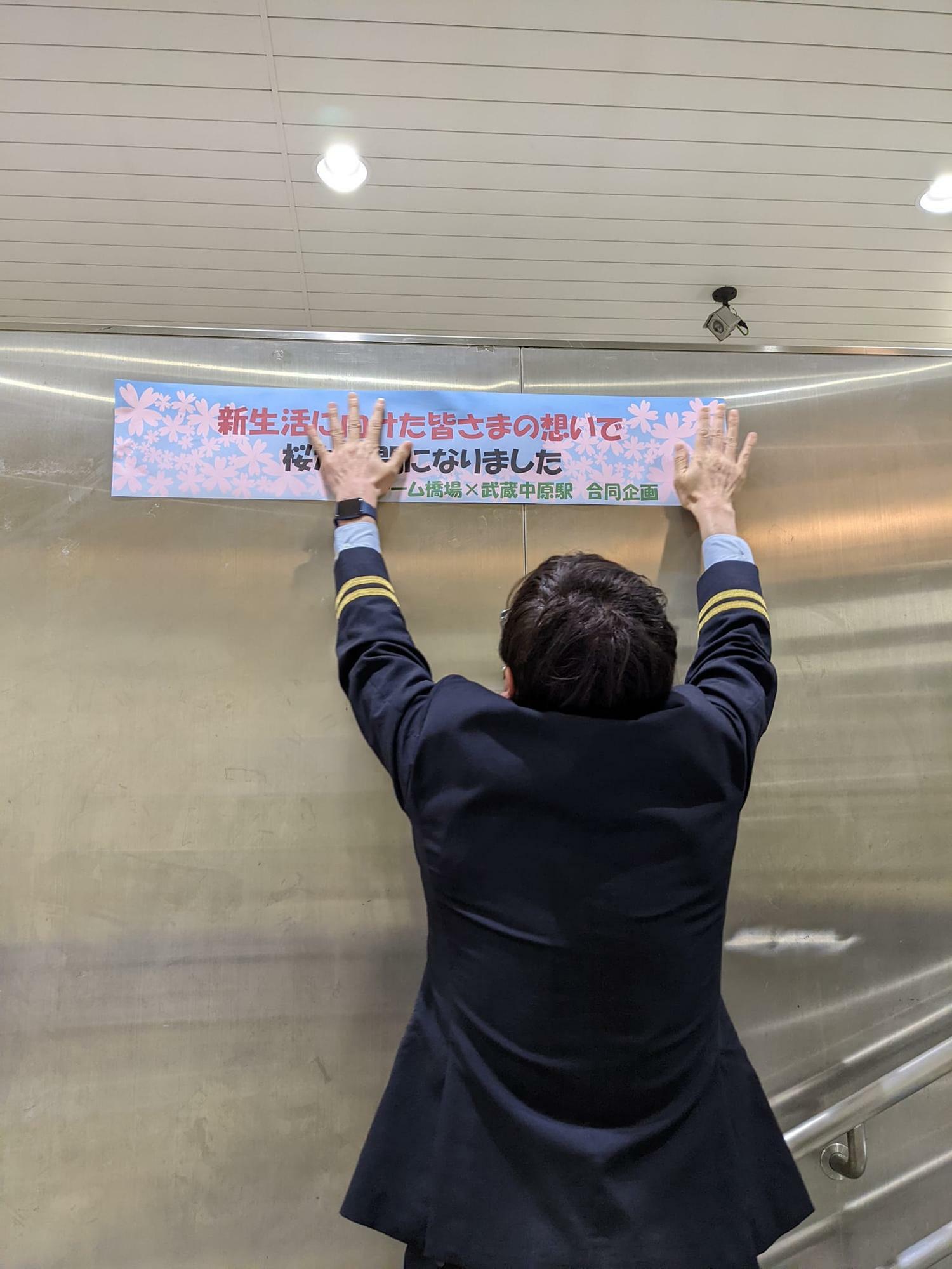 「チーム橋場」と武蔵中原駅の合同企画であることを知らせる掲示をペタリ。長身の松本駅長だからこそ、手が届く高さですね