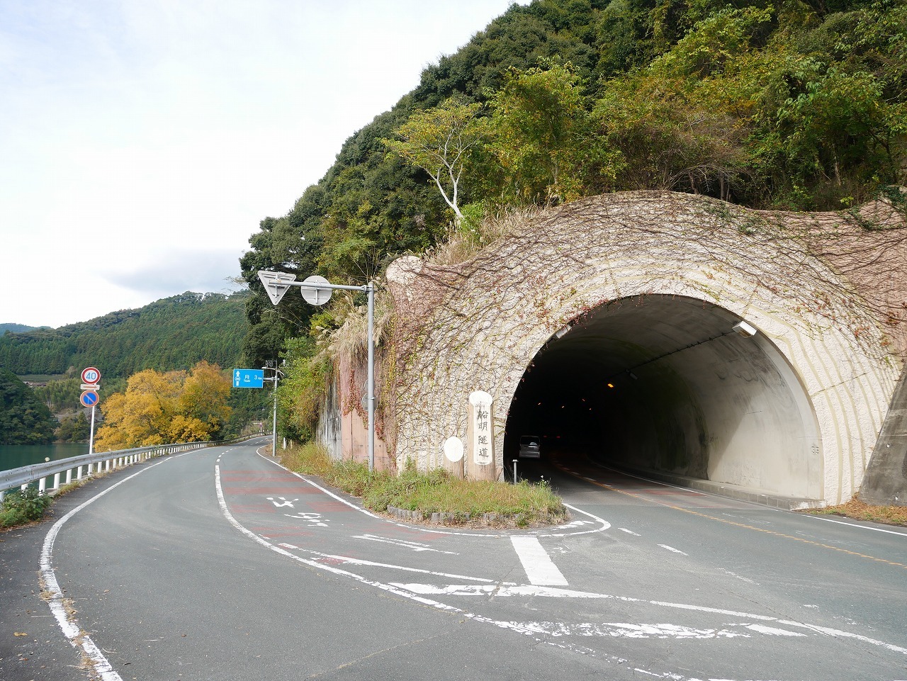 トンネルの脇に立つ有名な「月3キロ」道路案内板