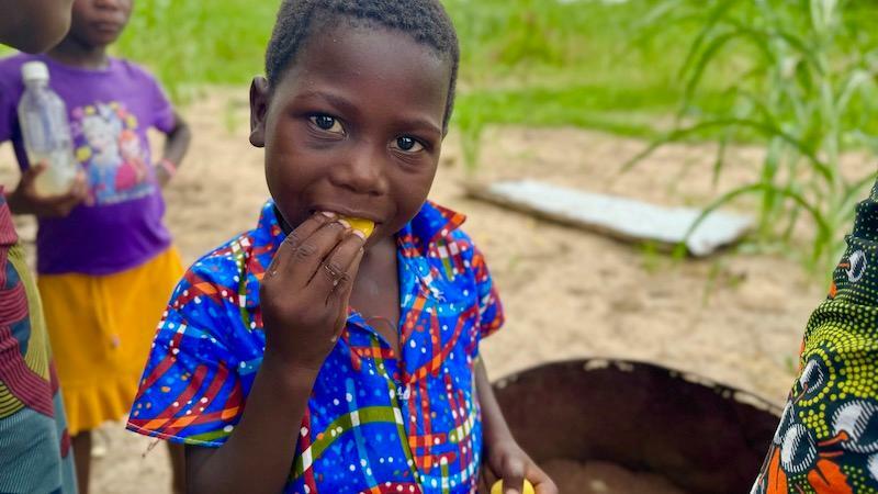 マルラの実を食べる現地の子ども。色鮮やかなアフリカ布で作られた洋服を着ている。