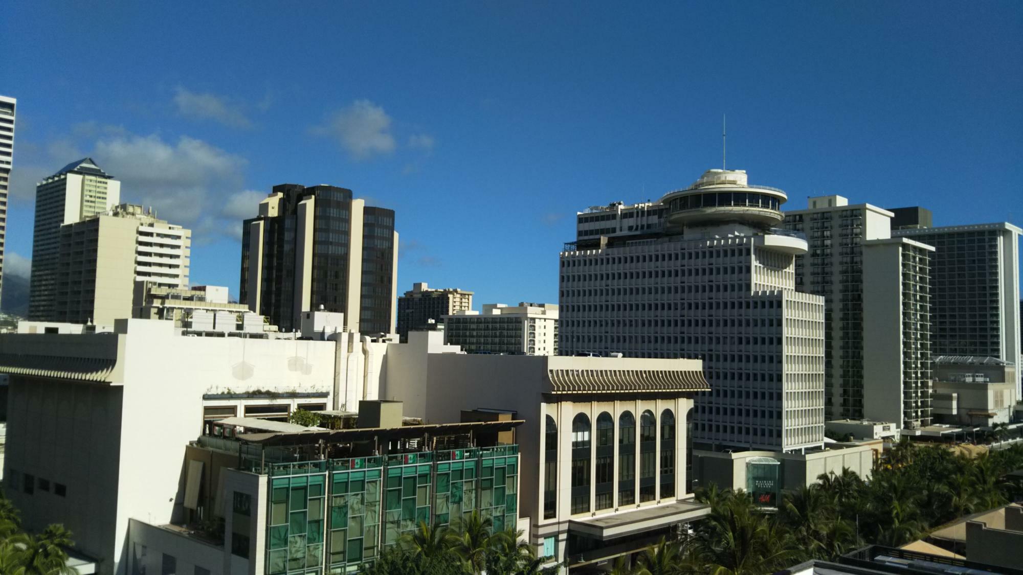 米国・ハワイ州ホノルル、ワイキキ。商業施設にビジネス街等が集中する人口密集地であるが、ダウンタウンではイオラニ宮殿やカメハメハ大王像で有名なハワイ州最高裁判所等、歴史的建築物も多い（2018年撮影）。