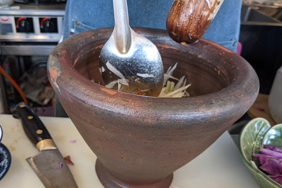 青パパイヤの料理、ソムタムを作る出河さん。クロック（鉢）はタイで使われている調理道具です。