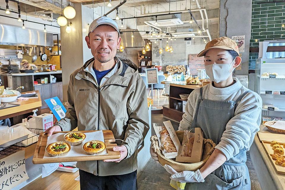 左：オーナーの浦本剛徳さんと「バターチキン納豆カレーパン」　右：ベーカリーリーダーの丹治智恵美さんと「納豆パニーニ」