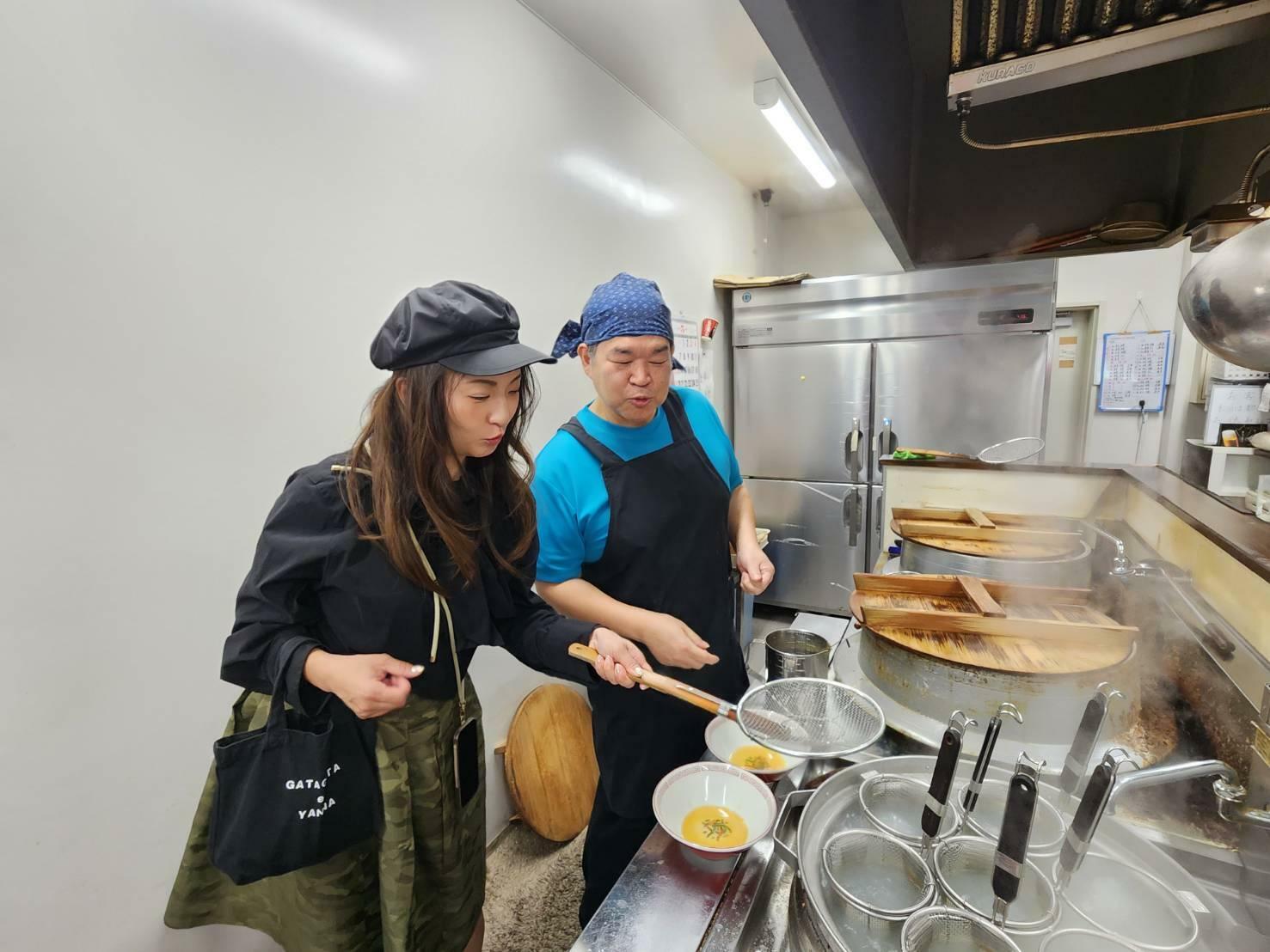 吉野会長から厨房に招かれ、ラーメンの製法を学ぶラーメン女
