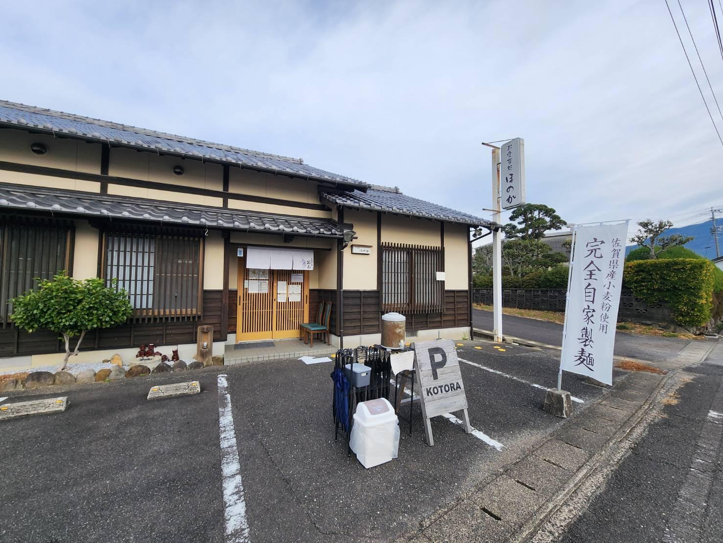 佐賀県・有田町にある「元祖佐賀つけ麺 孤虎佐賀本店」。以前あった食堂の看板をあえて残し、暖簾にだけ孤虎の屋号を入れている。順番待ちの客のため店前に日傘やウォーターサーバーを置く