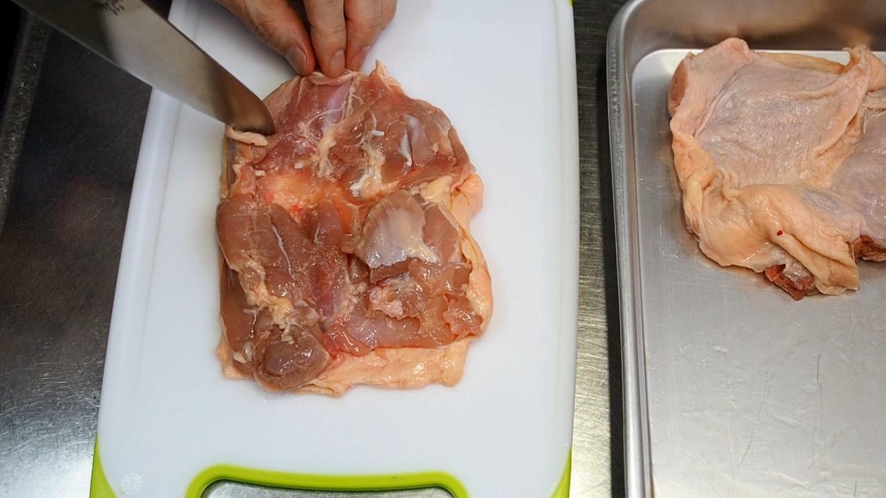 鶏もも肉ははみ出した油を切りとり、全体を包丁で刺して筋切ります。肉の繊維を切る方向に刺してください。