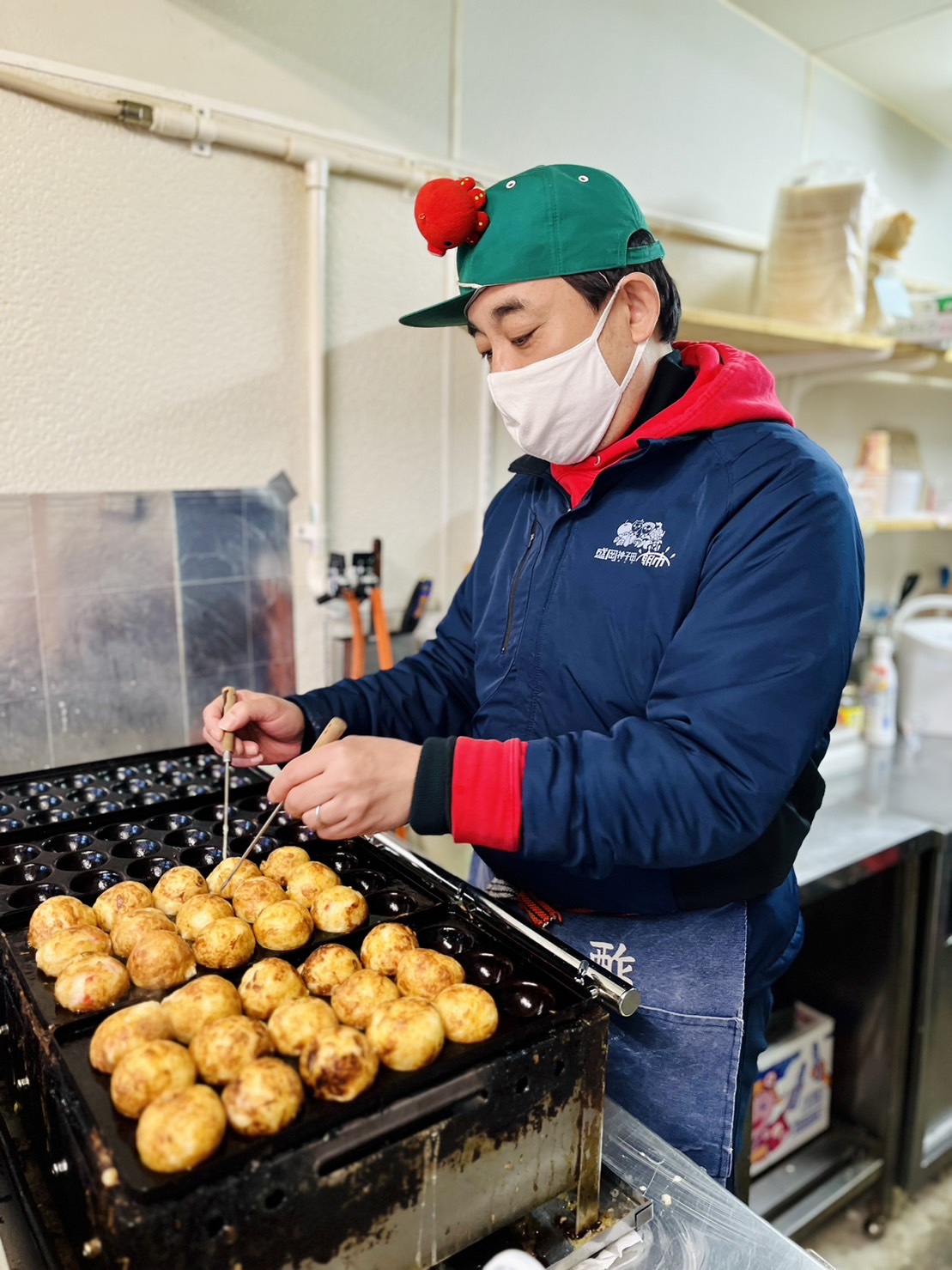 たこ焼きを焼く店主。朝市キャップにタコがついていてかわいい