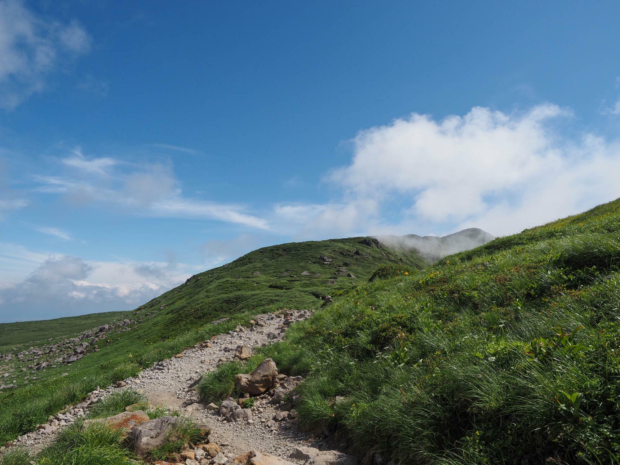 遠くにうすく雲がかかった月山の山頂を望む。