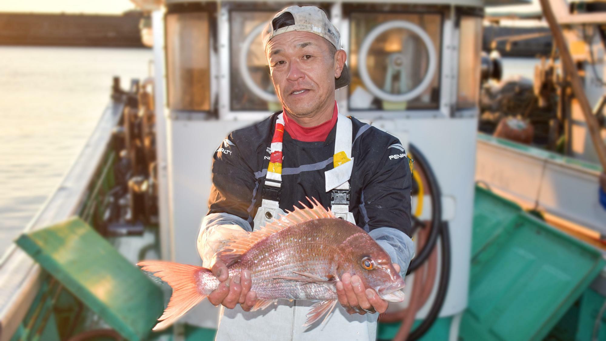 天然真鯛を手に持つ福間漁港の漁師さん　提供：(一社)福津いいざい