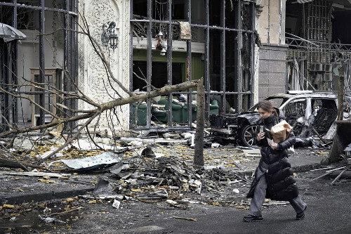 キーウで、ロシアの攻撃で破壊された建物の前を通り過ぎる女性