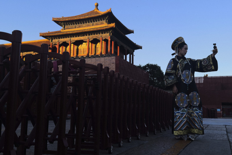 中国・北京で伝統的な清時代の衣装をまとった若者女性が自撮りをする様子。現代文化と歴史的要素の融合を示す。
