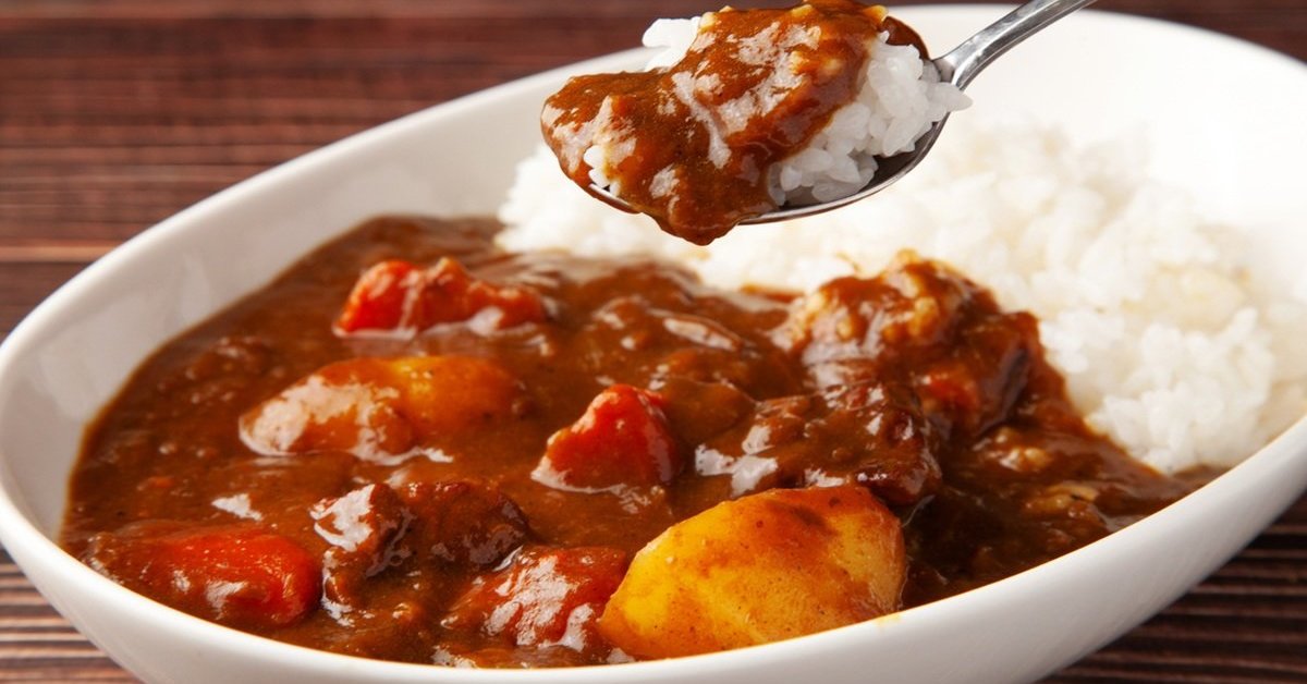 ご飯にカレールーをかける手元のクローズアップ。日本の多くのカレー店が厳しい経営状況に直面していることを示唆。