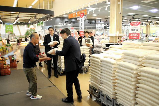 福島県郡山市のヨークベニマル店舗で、スタッフが買い物客に政府備蓄米を手渡す様子。静かに販売が開始された初日の光景。