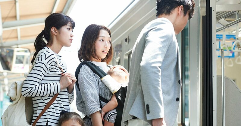 混雑した駅のホームで電車を待つ人々。整列乗車を促す標識も見える。