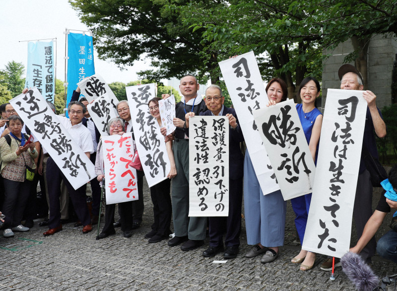 最高裁判決後、「勝訴」の紙を掲げる生活保護受給者の原告団