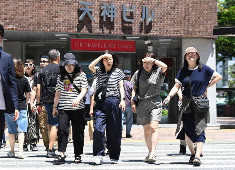 九州北部で記録的最速の梅雨明け後、強い日差しの中を歩く人々