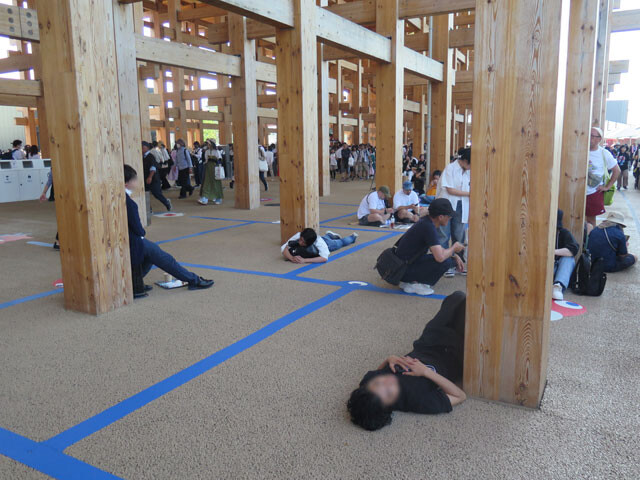酷暑の大阪・関西万博会場、大屋根リング下で暑さに疲れ寝そべる来場者たち