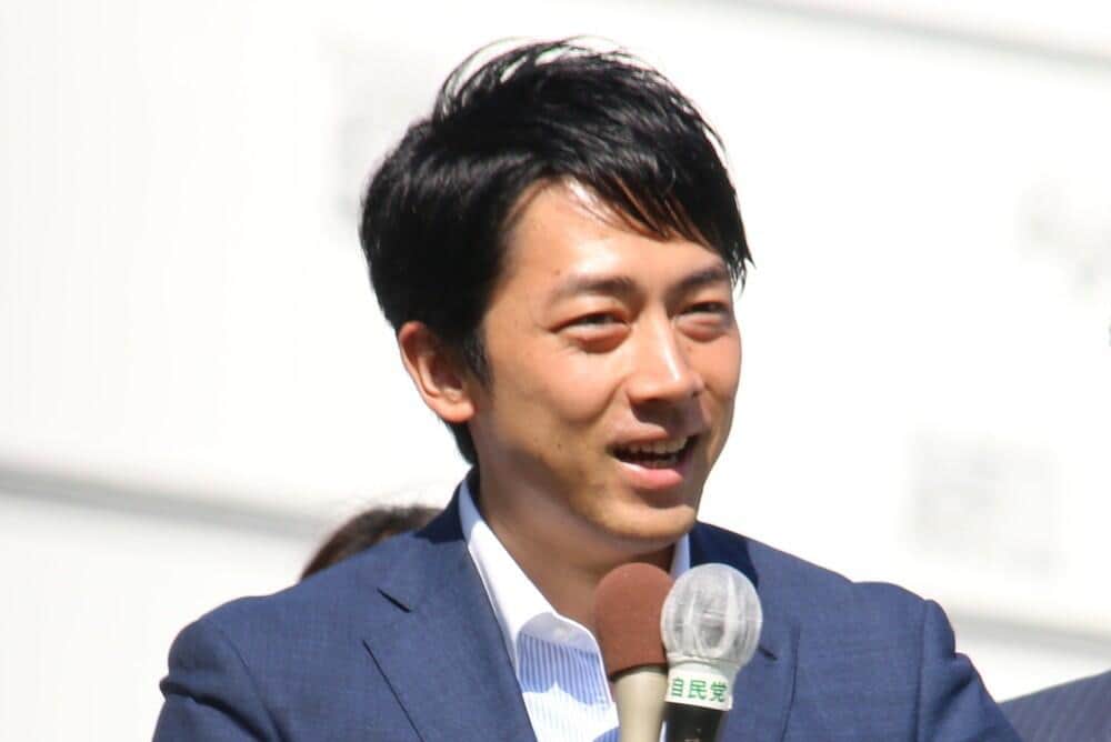参院選応援のため移動中の機内で、紙の新聞を手に窓の外を見る小泉進次郎農水大臣。座席脇には他の新聞も積まれている。