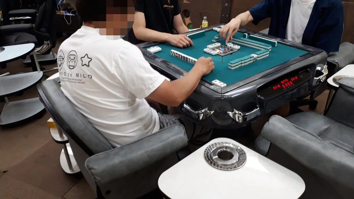 マンションの一室で麻雀を打つ男性3人。高レート賭博の雰囲気を伝える写真。