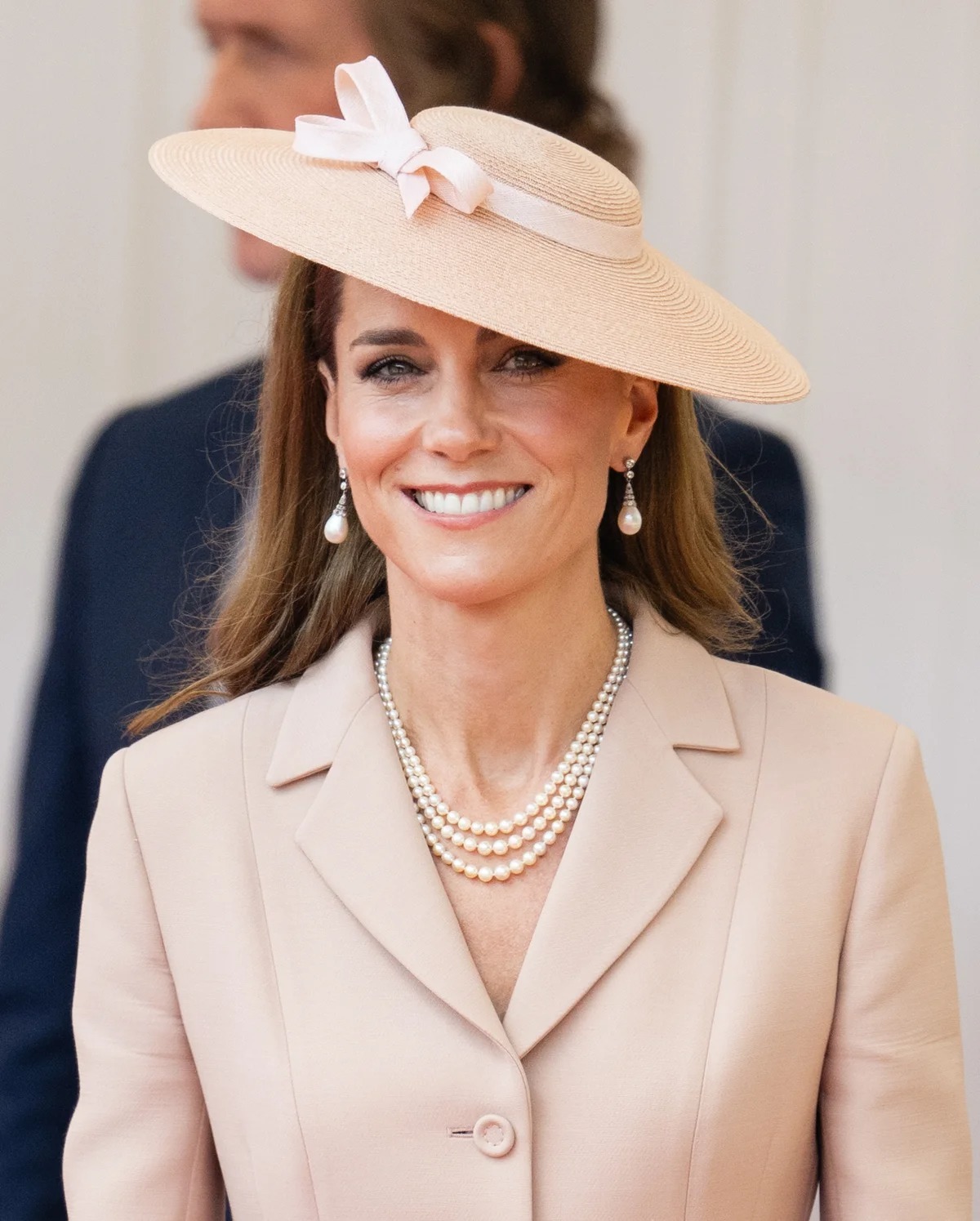キャサリン皇太子妃が、フランスのエマニュエル・マクロン大統領夫妻歓迎式典でペールピンクのディオールスーツを着用し、ウィリアム皇太子と並んで立つ姿。構築的なジャケットとチュールスカートが特徴的。