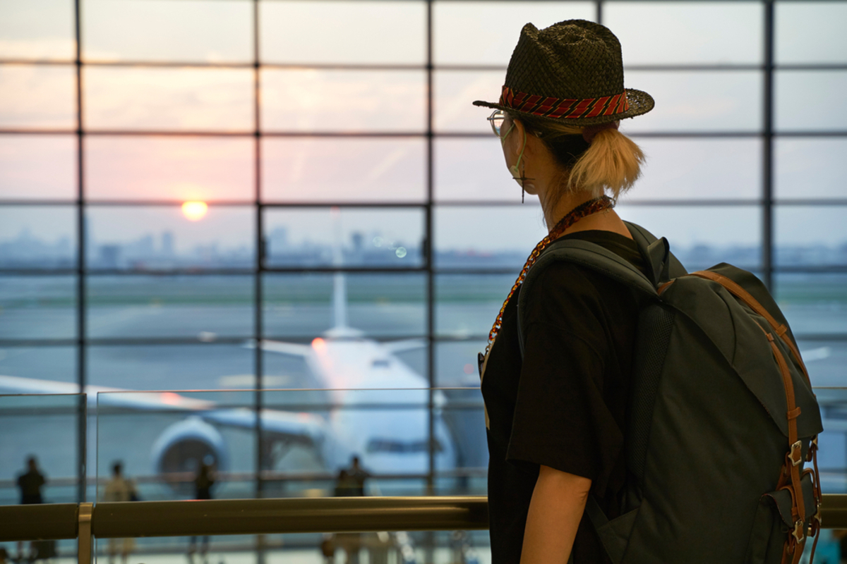 空港の窓から離陸する飛行機を眺める人物の横顔。年収と大手航空会社の利用頻度について考察するイメージ。