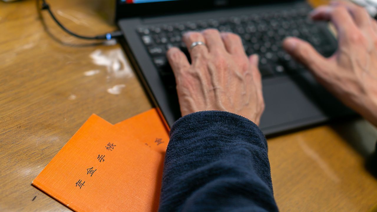 年金手帳と電卓、積み重ねられた小銭。老後の生活設計と年金受給額の計算の複雑さを示す。