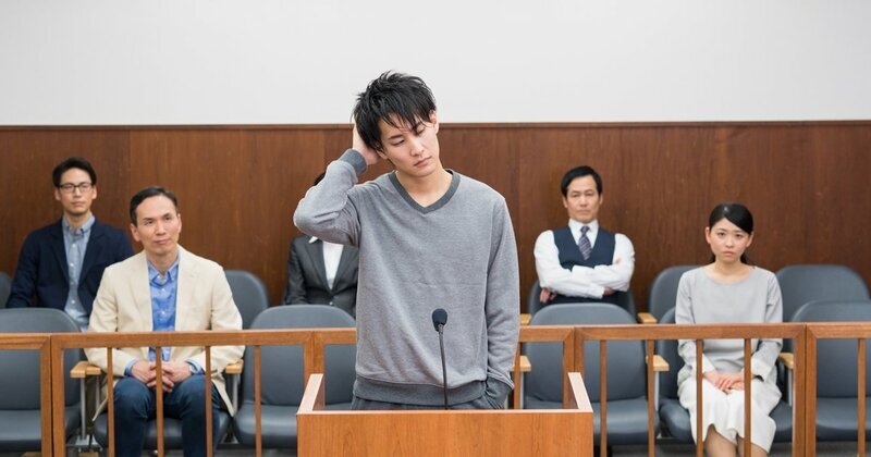 裁判官が判決文を作成するために机に向かい、六法全書や書類の山と向き合う様子