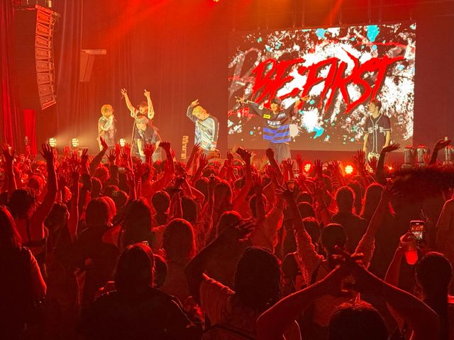 BE:FIRSTのパリ公演で、観客とメンバーが一体となって熱狂するライブ会場の様子。観客は笑顔でパフォーマンスに夢中になっている。