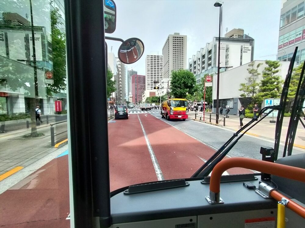大型バスが赤信号の手前でゆっくりと惰性走行する様子。後続の乗用車からは、大型車の運転手の意図が理解されにくいが、実は効率的な理由がある。