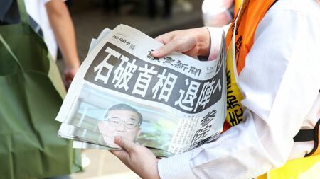 「石破首相 退陣へ」と報じる読売新聞の号外を手にする人物。首相の報道否定後、その背景が注目される政局の動きを示唆。