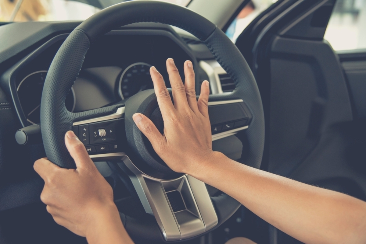 青信号で停止している車内で、クラクションの使用を検討するドライバーの視点。道路交通法による警音器使用のルールと罰則について示唆するイメージ。