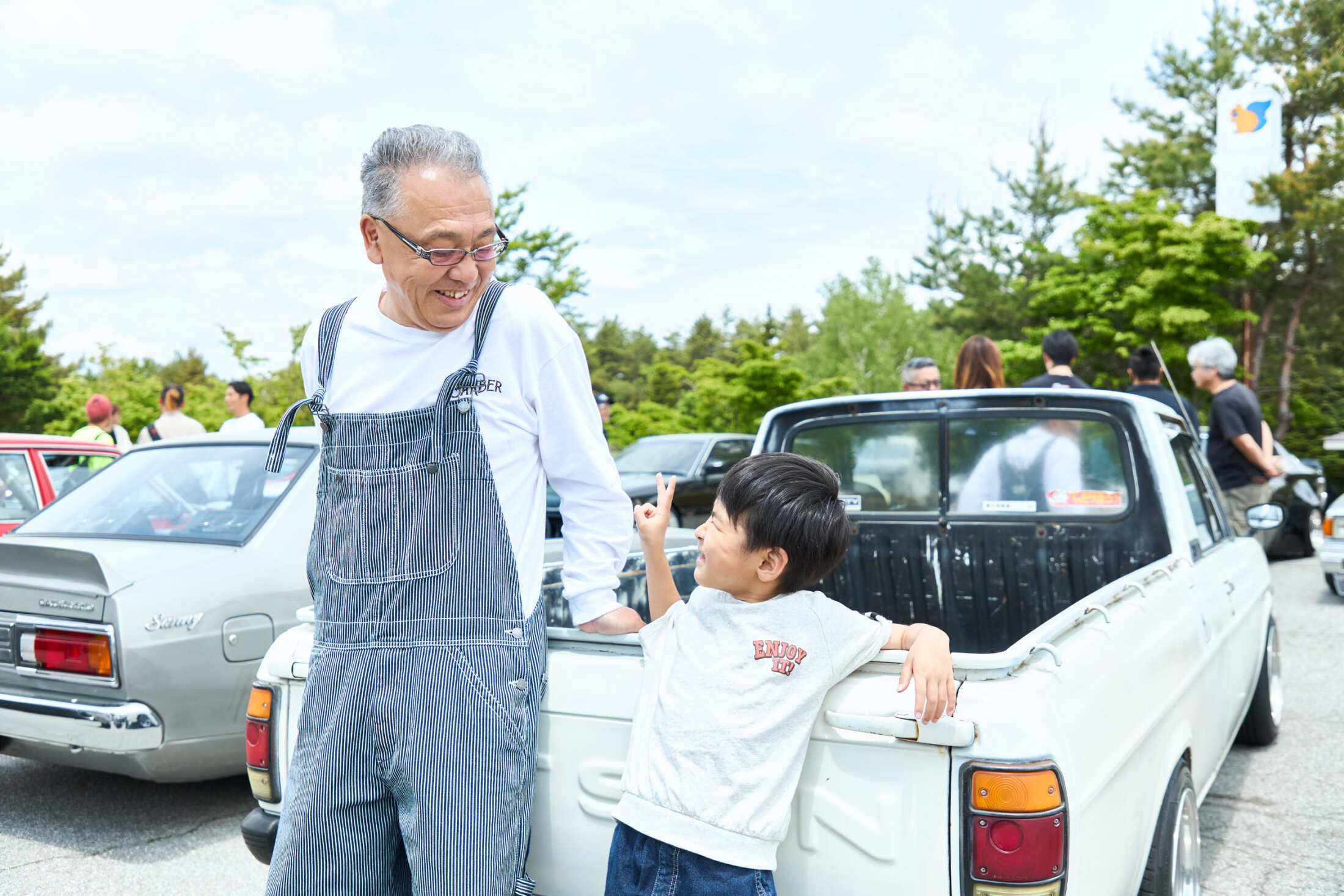 サニートラックの助手席で笑顔を見せる田中さんの孫と、愛車を前に語らう田中さん。旧車との温かい家族の絆を象徴する一枚。