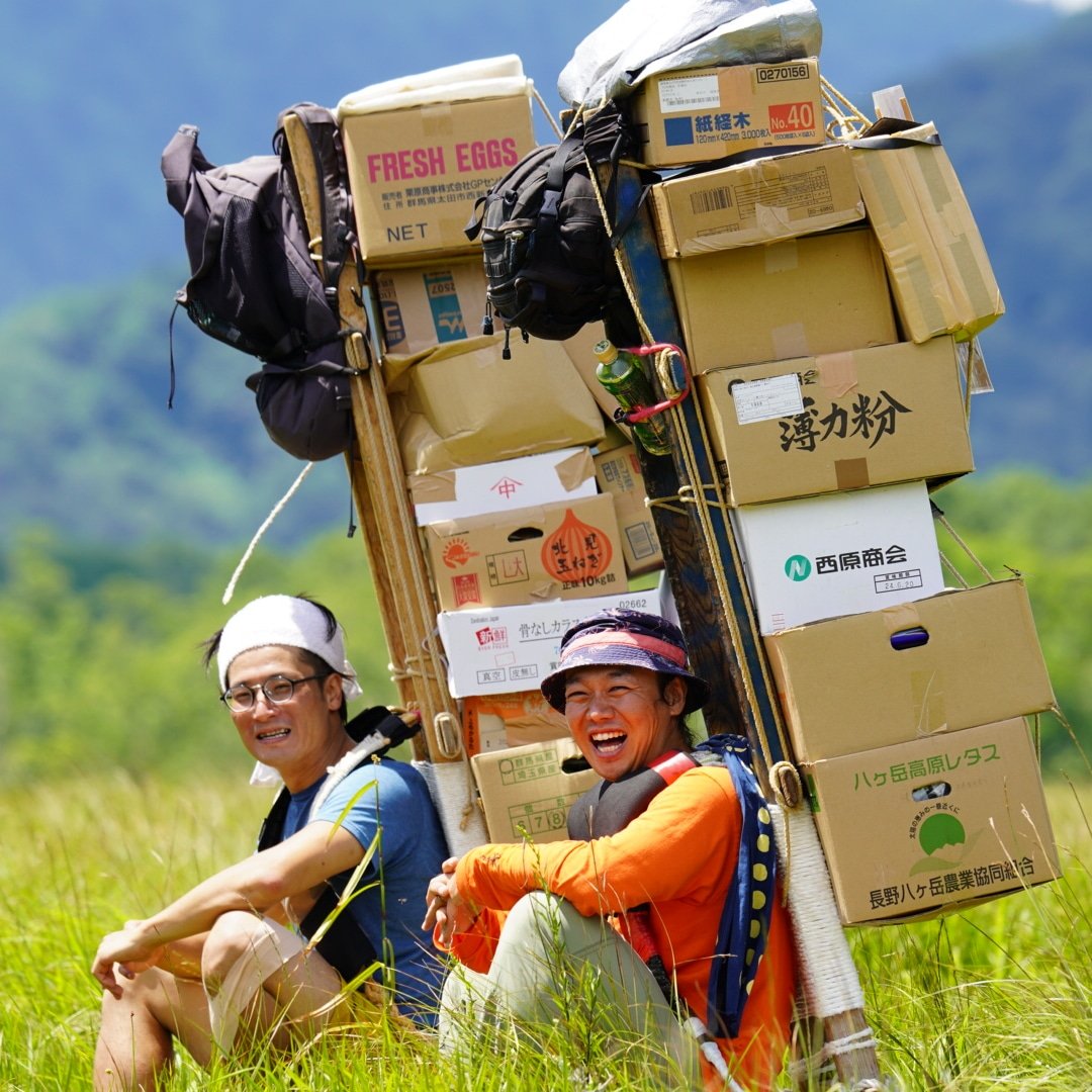 重い荷物を背負い、山道を歩く歩荷の姿