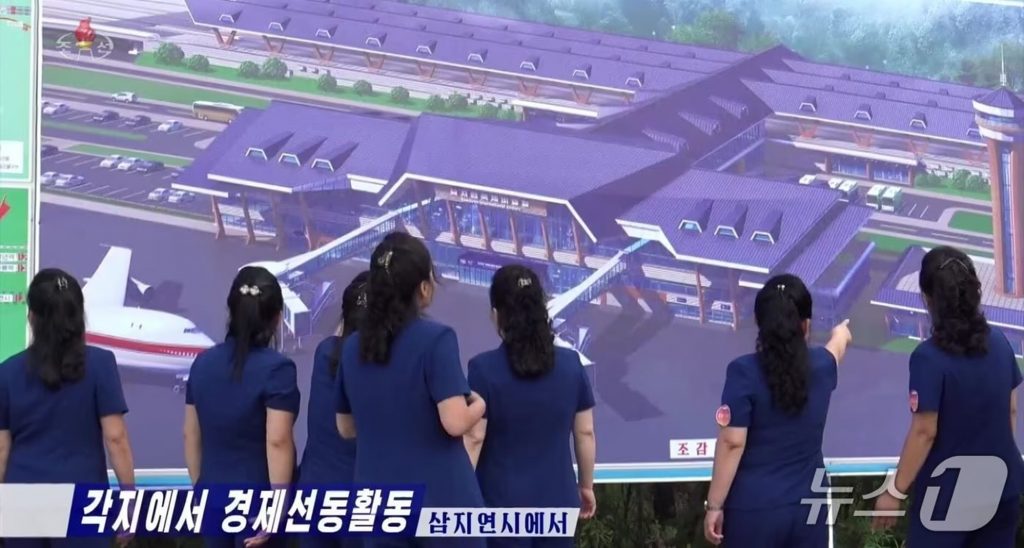 朝鮮中央テレビで公開された三池淵国際飛行場の複合型駅舎配置案と鳥瞰図の3Dレンダリング映像。背景に映る宣伝音楽隊とともに、北朝鮮の国際空港化計画を示す。