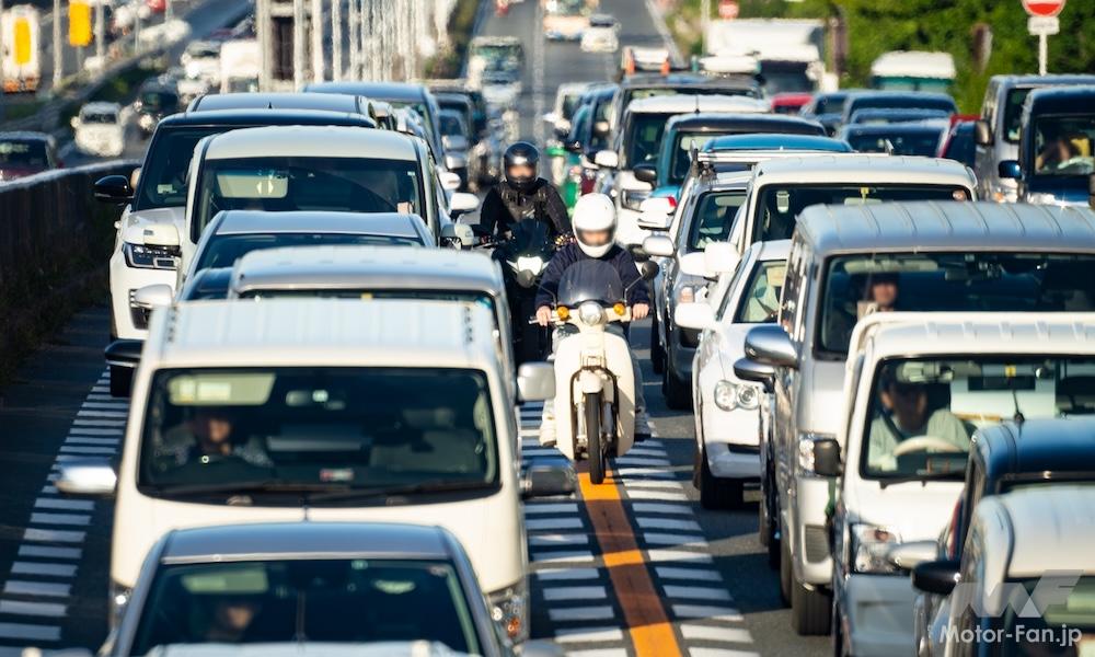 交通量の多い市街地で、車列の間をすり抜けるバイク。事故のリスクを伴う運転行為の例。