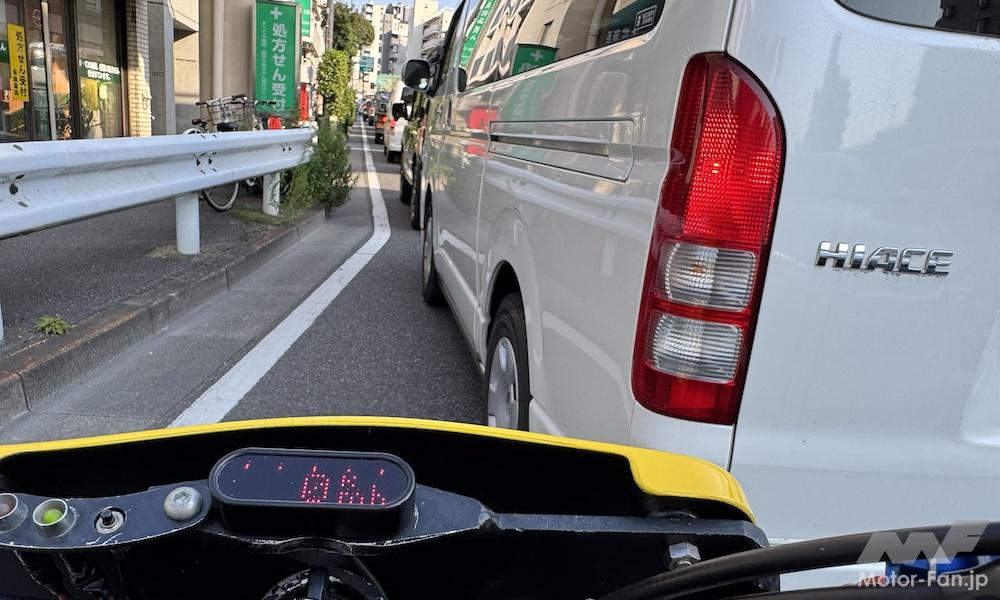 都市部の幹線道路で、停車中の車列の間を走行するバイク。すり抜けの危険性とライダーの注意喚起。