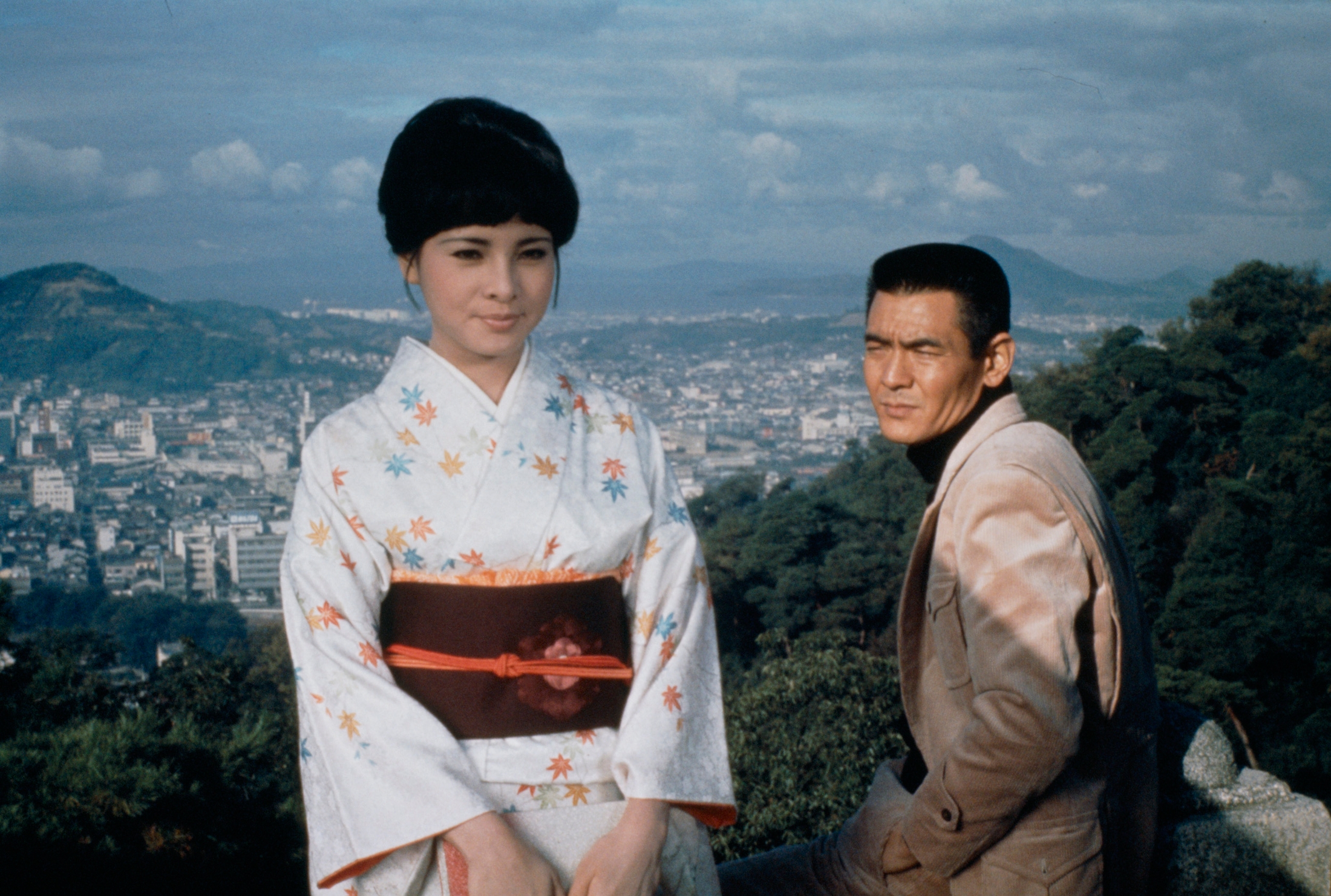 映画「トラック野郎 天下御免」のワンシーン。菅原文太演じる桃次郎と愛川欽也扮するジョナサンがトラックの運転席で並んでおり、シリーズのコミカルな魅力を表現している。
