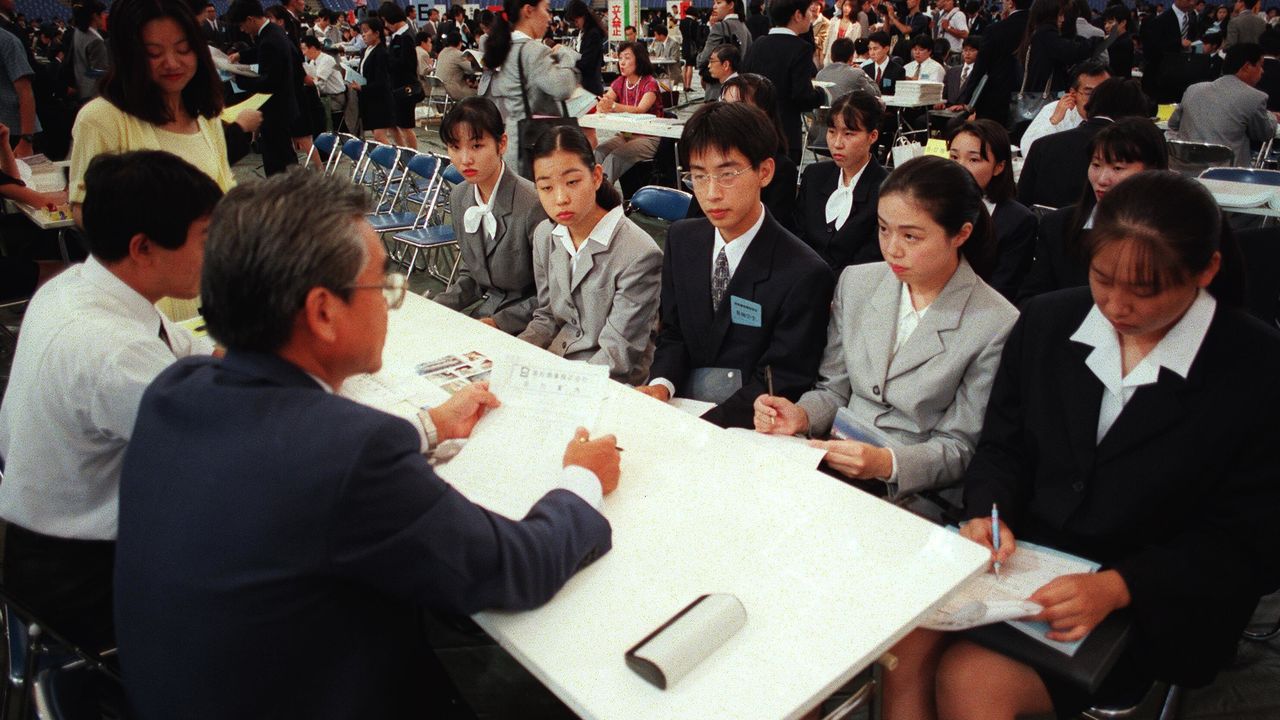 1995年、就職氷河期に東京ドームで行われた企業の合同面接会で説明を聞く学生たち。不況下での新卒採用市場の厳しさを象徴。