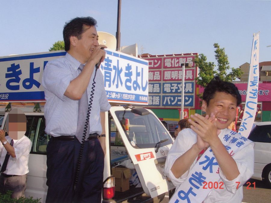 清水聖士元鎌ケ谷市長が民主党（当時）の菅直人代表（左）から応援演説を受ける様子。2002年7月、市長選の際に撮影された、若き日の市長と政治家の交流を示す貴重な一枚。