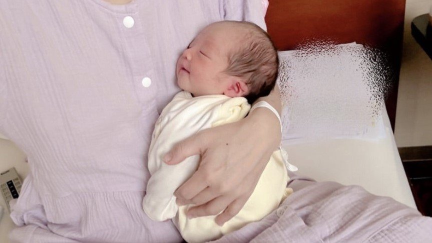 辻希美さんが新生児の第5子を抱きかかえ、優しい表情で見つめる姿。出産後の喜びが伝わる一枚。