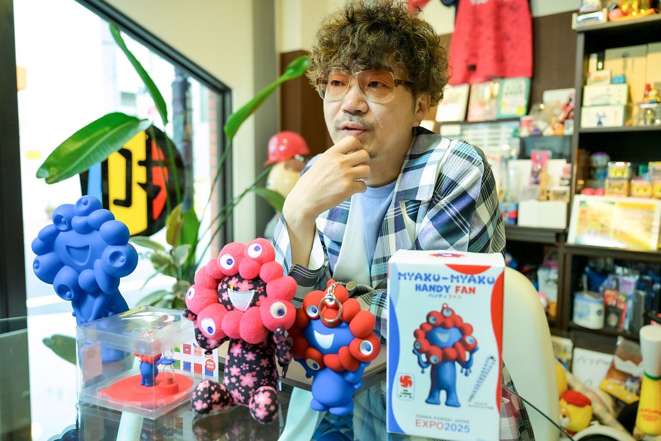 ヘソプロダクション代表の稲本ミノル氏がインタビューに応じる様子。彼のトレードマークであるグラサンとヒゲ、コムデギャルソンのスーツ姿が、第一印象戦略の重要性を物語る。