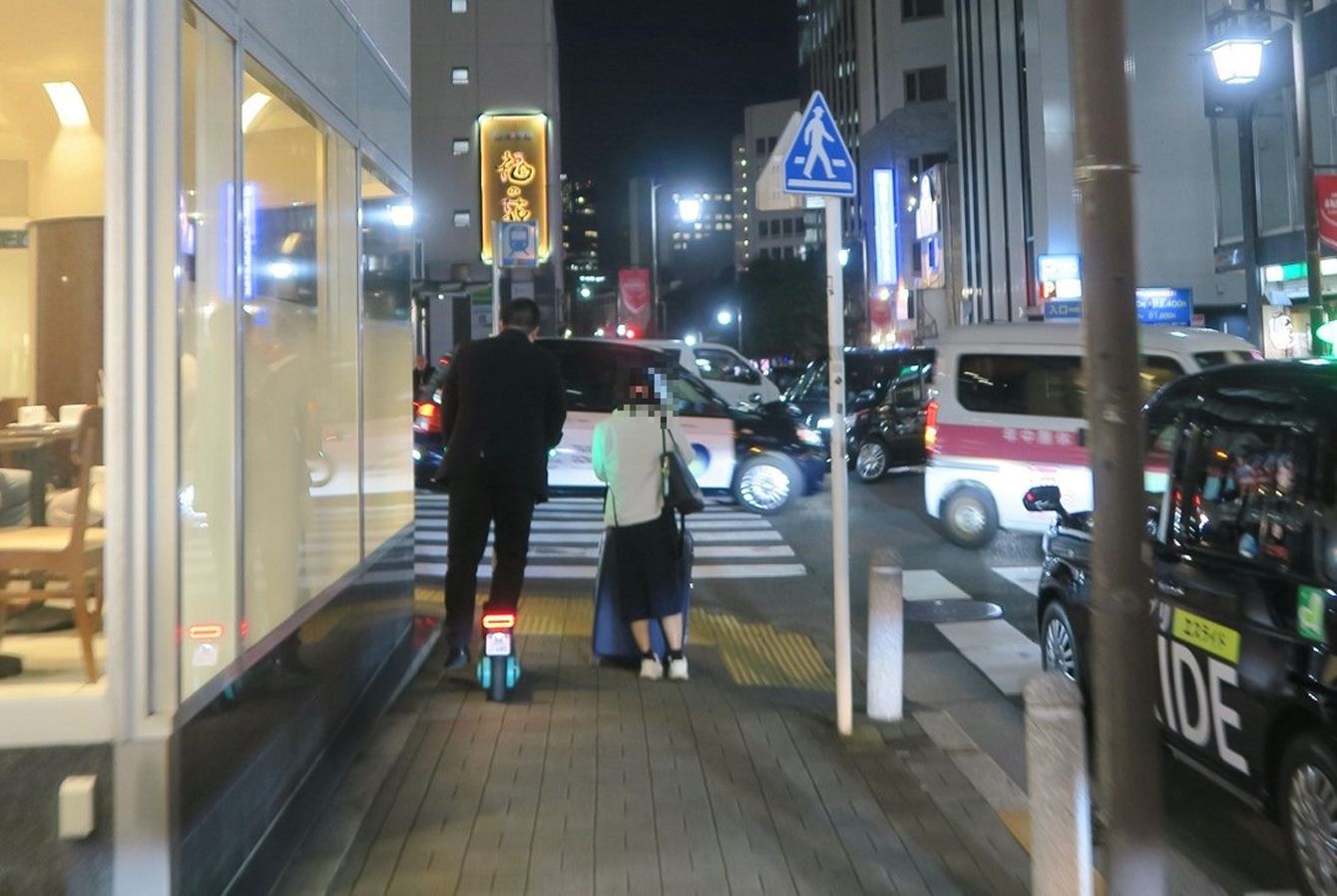 夜の繁華街で走行する電動キックボードLUUPの利用者。都市部の交通手段としての普及と、飲酒運転のリスクを想起させる光景。