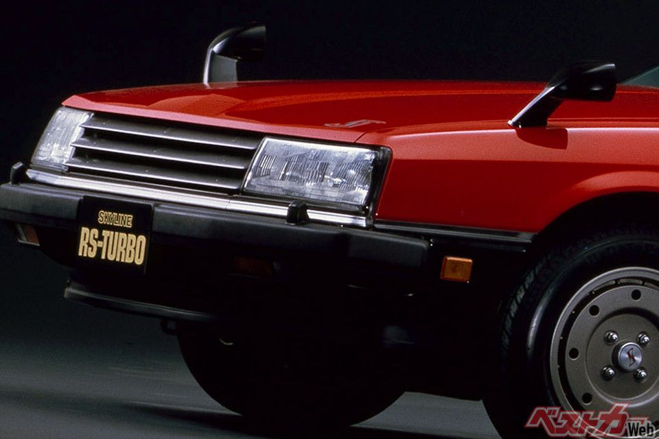 若き日の清水草一氏が愛車日産ガゼールを背景に立つ。60代の壁に直面するカーマニアの過去と現在を対比。