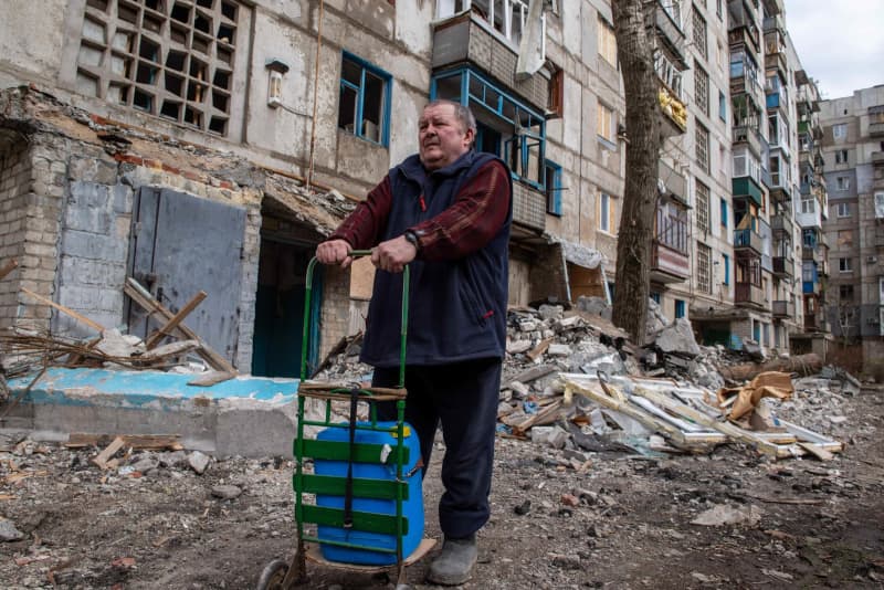ウクライナ東部ドネツク州北部で、破壊された集合住宅の前に立つ住民。紛争による深刻な被害と住民の苦境が垣間見える。