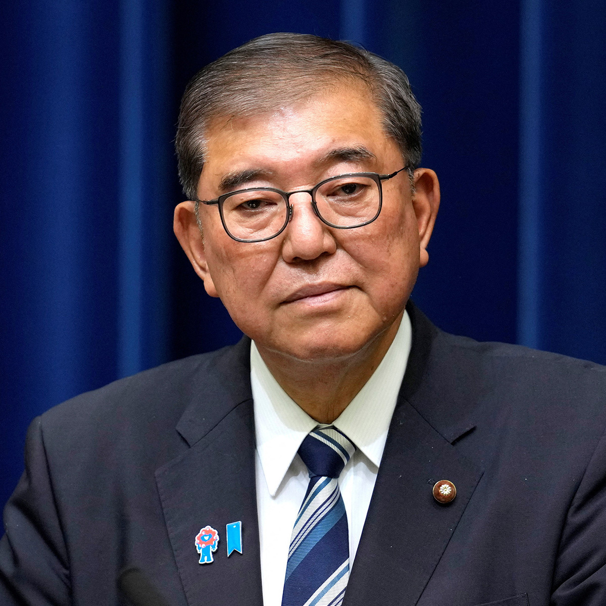 石破茂首相の辞任会見に臨む姿。紺色のスーツの襟元や胸元に多数の白い粒が付着しており、視聴者の間で「フケでは？」との声が上がった。