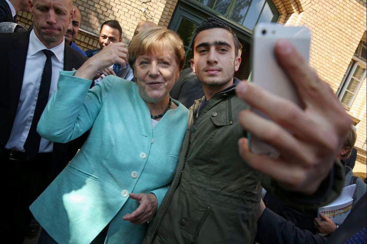 2015年、シリア難民アナス・モダマニさんと握手し、自撮り写真に応じるメルケル独首相