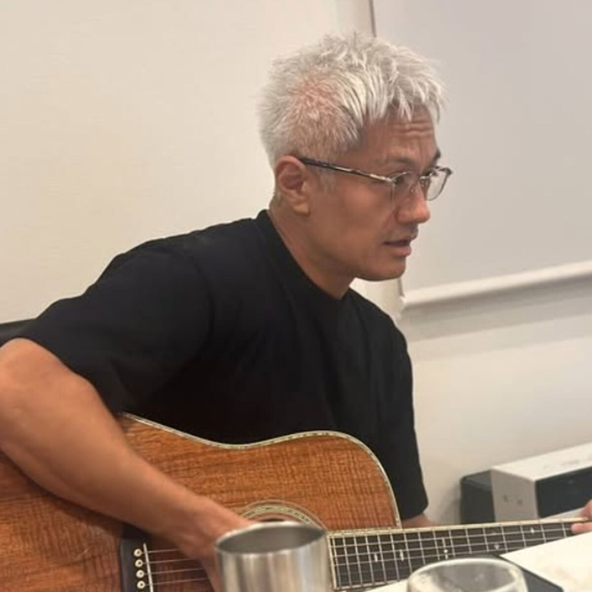 押尾学氏がギターを手に、自然に白くなったと語る髪と渋い表情を見せる。Instagram投稿より。