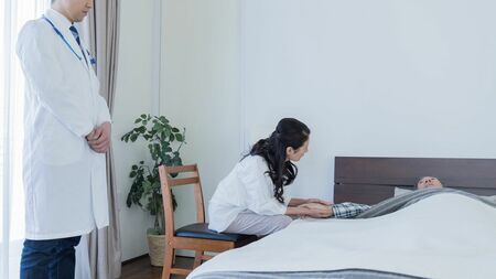 自宅で療養中の高齢者の手を優しく握る介護者の手